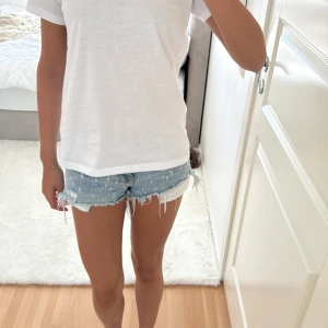 Blå jeansshorts från Bershka - Säljer ett par blå jeansshorts från Bershka med låg midja. De har slitna detaljer, fransig kant och klassisk femficksdesign. Dragkedja och knapp framtill. Perfekta för sommarens alla häng och riktigt snygga till en enkel t-shirt.