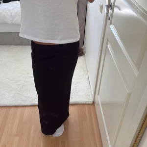 Svart ribbad långkjol med slits - Säljer en svart långkjol med ribbad struktur och en snygg slits bak. Kjolen sitter tight och har en enkel, stilren look som är lätt att matcha. Perfekt för dig som gillar minimalistisk stil och vill ha något bekvämt men ändå trendigt.