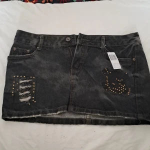 Svart jeans kjol yk2 style - Cool svart jeanskjol som är rätt så kort. Slitna detaljer och guld diamanter, (några har lossnat). Ena bak fickan är gul och brun. Köpt från en marknad i Thailand.