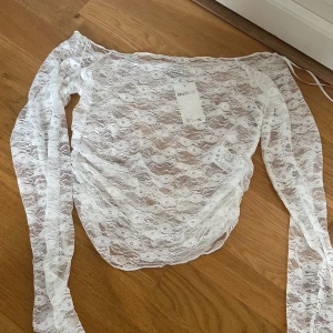 Vit spets off shoulder topp - Superfin vit blus i transparent spets. Toppen har långärmade offshoulder-ärmar och ett blommigt spetsmönster över hela toppen. Perfekt för dig som vill ha en romantisk och trendig look med lite edge. Säljes i storlek S.