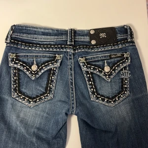 Lågmidjade Miss Me jeans med bling och bootcut - HÖR AV ER OM NI VILL KÖPA Säljer ett par blå jeans från Miss Me med snygga detaljer som blingade knappar och nitar på fickorna, samt kontrastsömmar. Modellen har bootcut och låg midja, vilket ger en cool och trendig siluett. Perfekt för dig som gillar statement-jeans med extra attityd.