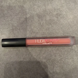 Huda Beauty Liquid Matte läppstift - Snyggt flytande matt läppstift från Huda Beauty i en mjuk nude-rosa nyans. Den är i färgen bombshell och är helt oanvänd. Nypris är 339.