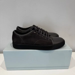 Mörkgrå sneakers från Lanvin  - Snygga mörkgråa sneakers från Lanvin med en stilren design. Skorna är mocka och har matt tå, samt matchande gråa snören. Kommer med originalkartong och extra skosnören. Ytterst sällan använda!