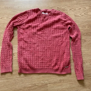 Rosa stickad tröja från Lexington - Säljer en snygg rosa stickad tröja från Lexington med kabelstickat mönster. Tröjan har rund hals, långa ärmad. Perfekt för dig som gillar klassisk stil med en färgklick.