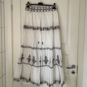 Vit långkjol med brodyr från Zara - Superfin vit långkjol från Zara med broderade detaljer i svart och beige. Kjolen har snörning i midjan med pärlor,,, en liten defekt på ena snöret (bild 2) men annars i bra skick!!!
