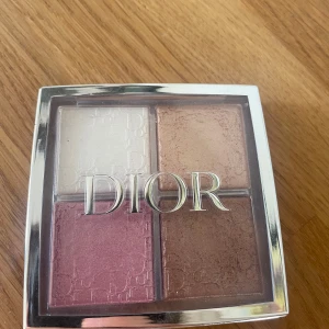 Dior highlighterpalett med fyra nyanser - Snygg highlighterpalett från Dior med fyra skimrande nyanser: pärlvit, champagne, rosé och bronzebrun. Kommer i en lyxig fyrkantig dosa med silverram och tydlig Dior-logga. Perfekt för att ge glow och lyster till ansiktet.