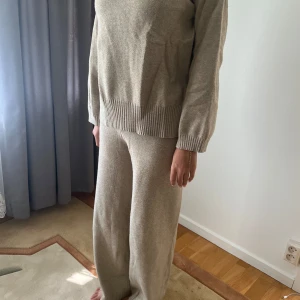 Beige stickad tröja med ribbad kant - Mysig beige stickad tröja med långärmad passform och bred ribbad kant vid nederdelen och ärmsluten. Tröjan har en loose fit och är perfekt för chill dagar. Materialet är mjukt och skönt, och färgen är neutral vilket gör den enkel att matcha.