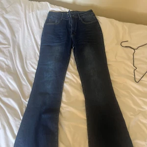 Bootcut jeans i mörkblå denim - Snygga bootcut jeans i mörkblå denim med klassiska fem fickor och kontrastsömmar. Byxorna har hög midja, dragkedja och två silverfärgade knappar framtill. Perfekt passform och coolt snitt som ger en retrovibe.