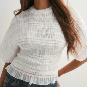 Vit blus med volang och rynk - Supersöt vit blus med rynkad struktur och volangkant nedtill. Blusen har korta, lite fladdriga ärmar och en hög halsringning. Storlek XXS (köpte två olika storlekar). Pris kan diskuteras vid snabb affär😊