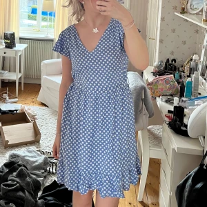 Blå prickig klänning med volang - Supersöt blå klänning med vita prickar och volangkant längst ner. Luftig och skönt material!! Snöre i midjan som knyts som rosett baktill/framtill!! 