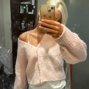 Ljusrosa croppad kofta med knappar nakd  - Supermysig ljusrosa kofta med bred ribbstickning och tre knappar framtill. Modellen är croppad och har långärmade, lite loose ärmar. Sitter snyggt offshoulder och är perfekt för dig som gillar en chill och söt vibe. Materialet är stickat och känns fluffigt.