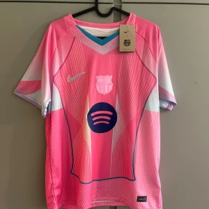 Barcelona Lamine Yamal rosa matchtröja - Snygg Barcelona fotbollströja med Lamine Yamal och nummer 10 på ryggen. Tröjan är rosa med vita och lila detaljer, har korta ärmar och coola grafiska linjer framtill. Nike-logga och Spotify-sponsor på bröstet. Tillverkad i lätt och ventilerande polyester.