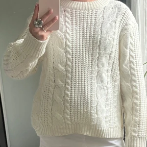 Vit stickad tröja med knappar - Säljer en chunky vit stickad tröja med grova flätstickade detaljer och snygga träknappar på sidan. Tröjan har rund hals och långa ärmar med breda muddar!🫶🏻