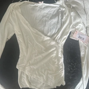 Vit omlottopp från Nelly i M - Supersnygg vit omlottopp från Nelly i mjukt och tunt material. Toppen har långa ärmar och en v-ringad omlottdesign som ger en clean och fräsch look. Perfekt att styla med jeans eller kjol för en trendig vibe.kan gå ner i pris det är bara att höra av dig ☺️