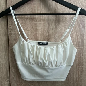 Vit croppad linnetopp från SHEIN - Fräsch vit linnetopp från SHEIN med smala axelband och snygg rynkad detalj framtill. Croppad passform som ger en trendig look, perfekt till jeans eller kjol. Mjukt material och justerbara band för bästa komfort.