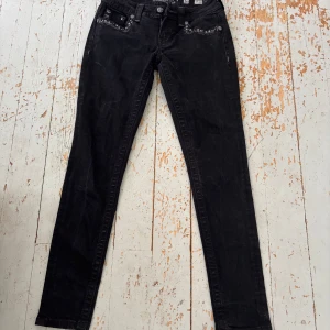 Svarta Miss Me jeans med dekorerade fickor - Snygga svarta jeans från Miss Me med skinny passform. Jeansen har coola detaljer med pärlor och broderier på både fram- och bakfickor, samt logotypen broderad i vitt. Materialet är klassisk jeans och de har normal midja. Perfekt för dig som gillar statement-plagg!