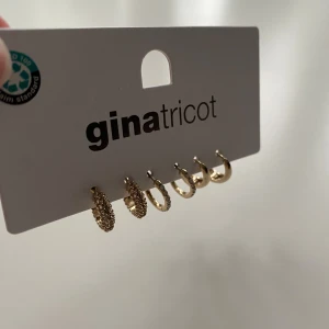 Guldiga örhängen från Gina Tricot - Tre par små hoops i guld från Gina Tricot. Ett par har en cool textur med pärldetaljer, ett par är glittriga med stenar och ett par är släta och blanka. Perfekt för att mixa och matcha flera hål i öronen och skapa din egen vibe. Nypris 149kr