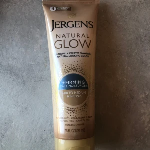 Jergens Natural Glow Firming - Jergens Natural Glow Firming är en daglig fuktkräm som gradvis ger en naturlig solkysst färg. Passar ljus till medium hudton. Innehåller kollagen och elastin, är parabenfri och cruelty free. Tuben rymmer 221 ml och har en beige och guld design. Använd endast en gång i en liten mängd. 
