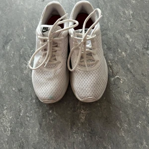 Vita mesh-sneakers från Nike - Fräscha vita sneakers från Nike med mesh-överdel och klassisk logga på plösen. Skorna har rund tå, platt sula och snörning. Perfekta för dig som gillar sportig stil och vill ha något lätt och luftigt på fötterna.