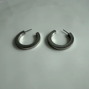 Silverfärgade hoops örhängen - Säljer ett par hoops örhängen i silverfärg med rund och tjock form. De har en stilren och minimalistisk look som passar dig som gillar att sticka ut med enkla detaljer. Perfekta för att ge din outfit lite edge.