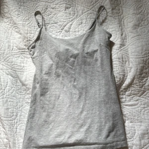 Grå linnetopp från Basic You XS - Snygg grå linnetopp från Basic You i ekologisk bomull. Modellen är enkel med smala justerbara axelband och rundad halsringning. Perfekt för dig som gillar en clean och chill stil. Passar dig som vill ha en basic topp i garderoben.