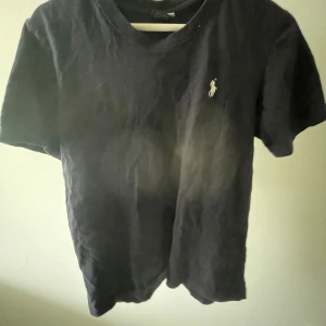 Svart t-shirt från Polo Ralph Lauren - Marinblå t-shirt från Polo Ralph Lauren i storlek S. Klassisk design med korta ärmar och rund hals. T-shirten har den ikoniska vita Polo-loggan broderad på bröstet. Tillverkad i mjuk bomull som är skön mot huden och passar perfekt till jeans eller shorts.