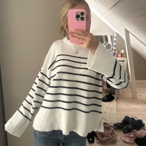 Vit randig stickad tröja - Vit stickad tröja med svarta horisontella ränder och bred ribbad kant vid ärmslut och nederkant. Modellen är loose fit med långa ärmar och rund halsringning. Perfekt för dig som gillar en chill och stilren look.