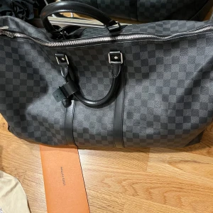 Louis Vuitton Keepall 55 Damier Graphite - Knappt använt min bag, den är som ny, har kanske 1-4 märken på den men de är knappast synliga. Kommer med allt, nycklarna, nyckellåset, dustpåsen till nycklarna, dustpåsen till väskan, boxen, brevet med kvitteringen. Köpt från LV butiken i Oslo.
