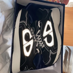 Svarta Dior B30 sneakers - Säljer ett par svarta Dior B30 skor med vita och silverfärgade detaljer. Skorna har en chunky vit och svart sula, reflekterande CD-logga på sidorna och bak, samt snörning i vitt. Aldrig använda bara testade.