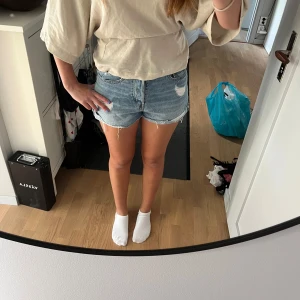 Jeansshorts  - Snygga blå jeansshorts med hög midja och fransig, sliten kant från HM. De har flera slitningar och hål. Klassisk femficksmodell med knappgylf. De är i  storlek 38