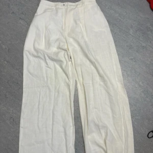 Vita linnebyxor med wide fit - Snygga vita linnebyxor med breda ben och relaxed passform. Byxorna har hög midja med dragkedja och knapp framtill samt resår baktill för extra komfort. Perfekta för en chill och stilren look under varma dagar.