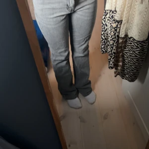 Grå bootcut jeans från Gina Tricot - Säljer ett par grå jeans från Gina tricot med bootcut passform. De har klassisk femficksdesign, midwaist. Jeansen är i mjukt denimtyg och har en snygg, ljusgrå tvätt som passar till allt. Perfekta för dig som gillar retrovibe och stilren look. Liten defekt på ena benet. Jag är ungefär 170 och de går ner under hälen. stl 36.