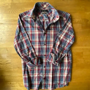 Rutig blå och röd skjorta från Riley - Snygg skjorta från Riley i slim fit med klassiskt rutig mönster i blått, rött och vitt. Skjortan har långa ärmar, knappar framtill och mjukt bomullsmaterial som känns skönt mot huden. Perfekt för dig som gillar en chill och stilren look.