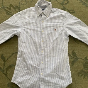 Randig skjorta från Ralph Lauren - Snygg slim fit skjorta från Ralph Lauren i vitt och blått med tunna ränder. Pris kan diskuteras. Perfekt till skolstart