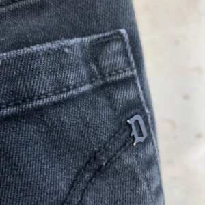 Svarta Dondup jeans med tryck - Säljer ett par svarta jeans från Dondup med coolt vitt tryck på linningen och metall-D-detalj vid fickan. Jeansen har klassisk femficksdesign, raka ben och är tillverkade i mjukt jeanstyg. Perfekt för dig som gillar street och snygga detaljer.