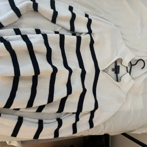 Vit och svart randig half zip tröja - Säljer en vit stickad tröja från H&M med svarta ränder och half zip vid halsen. Tröjan har långärmade ribbade ärmar och en hög krage. Perfekt för dig som gillar klassisk stil med en modern twist.
