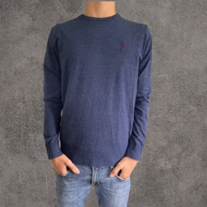 100% ull Blå slim fit tröja från Polo Ralph Lauren - Snygg marinblå långärmad tröja från Polo Ralph ull Lauren i slim fit med stretch. Tröjan har det klassiska röda broderade logotypen på bröstet och är perfekt för dig som gillar en stilren och enkel look. Tröjan har en lagning som verkligen inte syns vid användning 