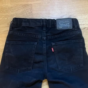 Levi's 510 svarta skinny jeans - Svarta Levi's 510 jeans med skinny passform och klassisk femficksdesign. Jeansen har en mörk ton, raka ben och är tillverkade i stretchigt denim för extra komfort. Märkespatch baktill och röd Levi's-tag vid bakfickan. Perfekt för en clean och stilren look.