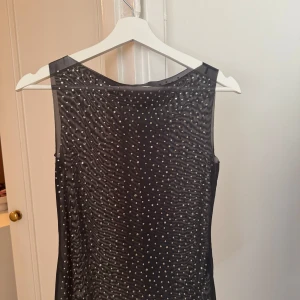 Mesh top weekday med stenar  - Supersnygg svart topp med glittriga detaljer över hela tyget. Ärmlös modell med rund halsringning och en smickrande siluett. Perfekt för dig som vill sticka ut med lite extra bling. Materialet känns lätt och följsamt mot kroppen.