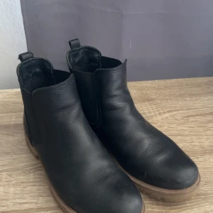 Svarta chelsea boots från Björn Borg - Snygga svarta chelsea boots från Björn Borg med rund tå och platt sula. Skorna är tillverkade i skinn och har elastiska paneler på sidorna för enkel påtagning. Perfekta för dig som gillar stilrena och klassiska boots med en modern touch.