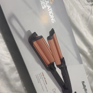 BaByliss vågtång koppar/svart - Säljer en BaByliss vågtång med snygga kopparfärgade plattor och svart handtag. Perfekt för att skapa stora, mjuka vågor i håret. Tången har flera värmeinställningar och kommer med ett värmeskyddande fodral. Stilren design och enkel att använda.