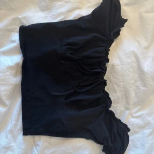 Svart offshoulder topp från SHEIN - Svart offshoulder topp från SHEIN med snygga volangdetaljer längs axlarna och en cool snörning framtill. Croppad passform som ger en trendig vibe. Tillverkad i mjuk bomull som känns skön mot huden. Perfekt för dig som gillar att sticka ut med din stil.