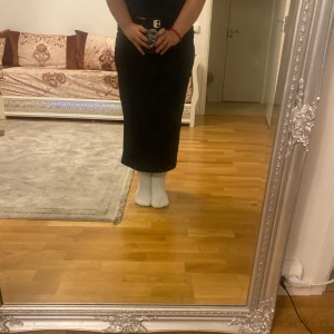 Svart långkjol med tight passform - Säljer en svart långkjol med rak och tight siluett. Kjolen är enkel och stilren utan synliga detaljer eller mönster, perfekt för dig som gillar minimalistisk stil. Passar dig som vill ha en klassisk look med en smickrande form.