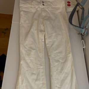 Vita bootcut jeans från H&M - Snygga vita bootcut jeans från H&M med låg midja och justerbar midja. Byxorna har klassiska fickor fram och bak, två silverfärgade knappar och är tillverkade i en mjuk bomullsblandning med lyocell och elastan för extra komfort.