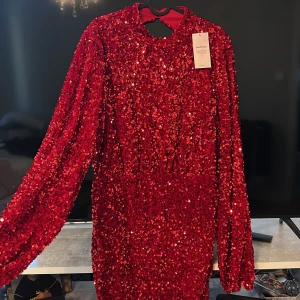 Röd paljettklänning från Nelly - Holiday Sparkle Dress från Nelly i intensivt röd färg, täckt med glittrande paljetter. Klänningen har lång ärm, rund hals och en snygg öppen rygg. Kort modell med figurnära passform, perfekt för att sticka ut på festen. Materialet är polyester, kortklänning och passar super till nyår och köptes för 800kr. 