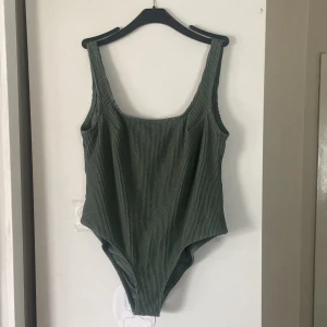 Grön ribbad baddräkt från H&M - Snygg grön baddräkt från H&M i storlek 46. Modellen har breda axelband, fyrkantig ringning och ribbad struktur i tyget. Tillverkad i stretchig polyesterblandning för en bekväm passform. Perfekt för strand eller poolhäng!
