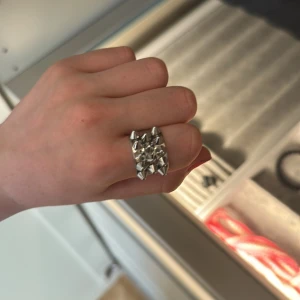 Bred silverring med nitar från Edblad  - Cool och chunky silverfärgad ring med rektangulär form och flera små nitar som ger en edgy vibe. Perfekt statement piece för dig som gillar att sticka ut och vill ha något unikt på fingret.