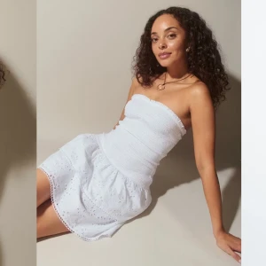 Vit axelbandslös sommarklänning - Supersöt vit kort klänning med smockad överdel och volangig kjol. Axelbandslös modell med broderade detaljer och hålmönster, perfekt för varma dagar. Lätt och luftig känsla. Storlek M men passar även S