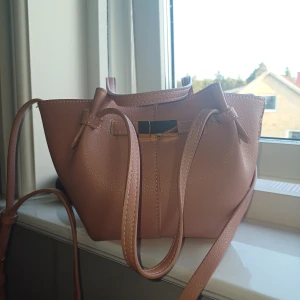 Rosa axelväska med gulddetaljer - Säljer en snygg rosa axelväska från lindex med guldfärgade detaljer och dragkedja på insidan. Väskan har långa axelband. Perfekt för dig som vill ha en trendig och praktisk väska till vardagen.