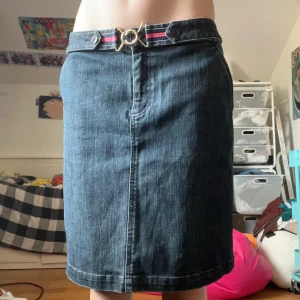 Mörk jeanskjol från Talbots med bälte - Snygg mörkblå jeanskjol från Talbots med rak passform och midjebälte med guldfärgat spänne och röd/vit rand. Kjolen har klassisk jeanslook, knappdetaljer i midjan och en bakficka. Perfekt för dig som gillar stilren denim.
